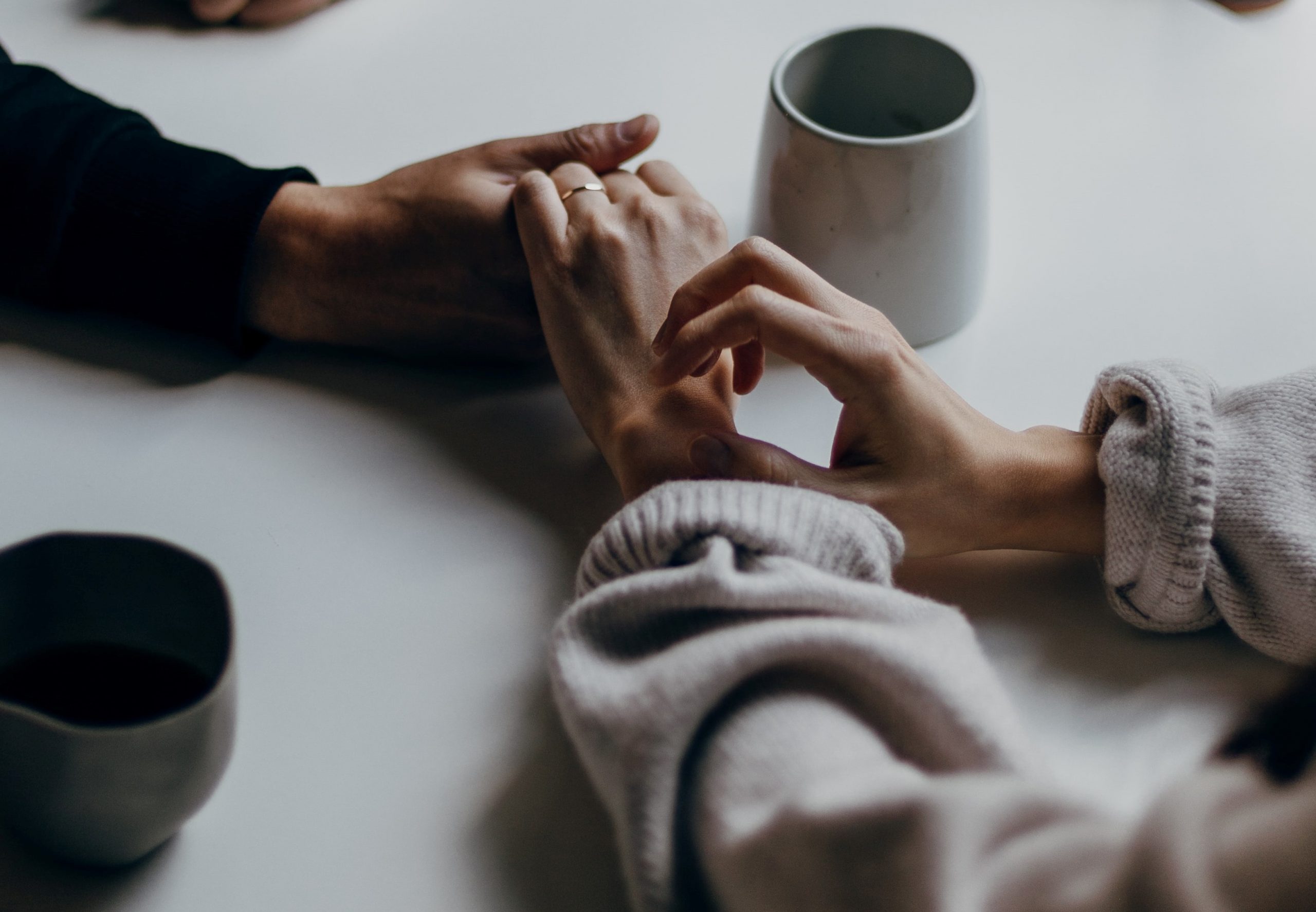 two people holding hands on a table with mugs on it