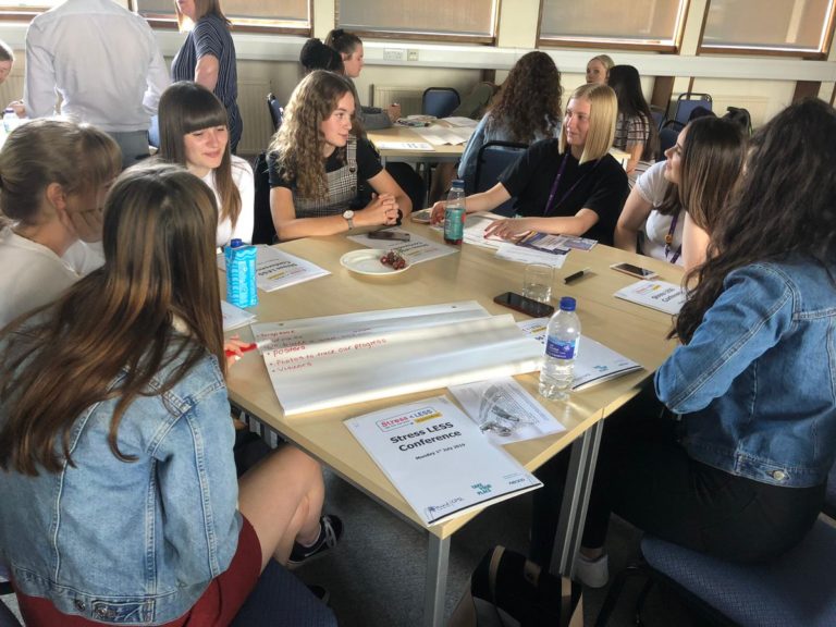 A group of women sat at a table talking at the Stress LESS Conference