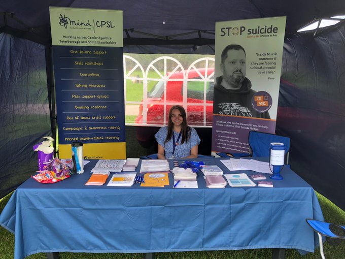 Brunette woman sat behind a table with two banners for CPSL Mind and Stop Suicide