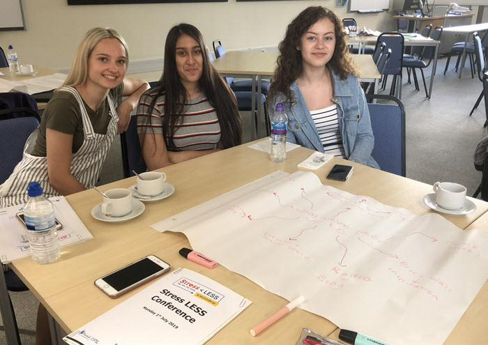 Three women sat at a table smiling at the Stress Less conference