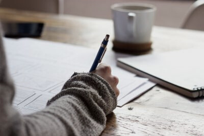 Person sitting at a wooden table writing with a pen on a piece of paper