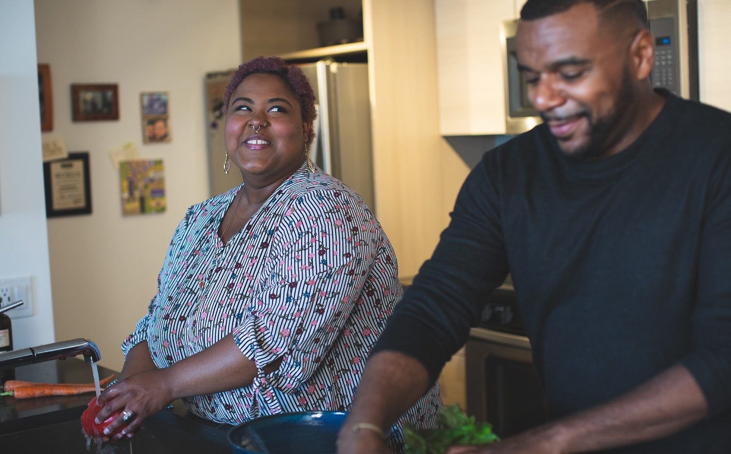 A man and a woman smiling at each other while doing the dishes