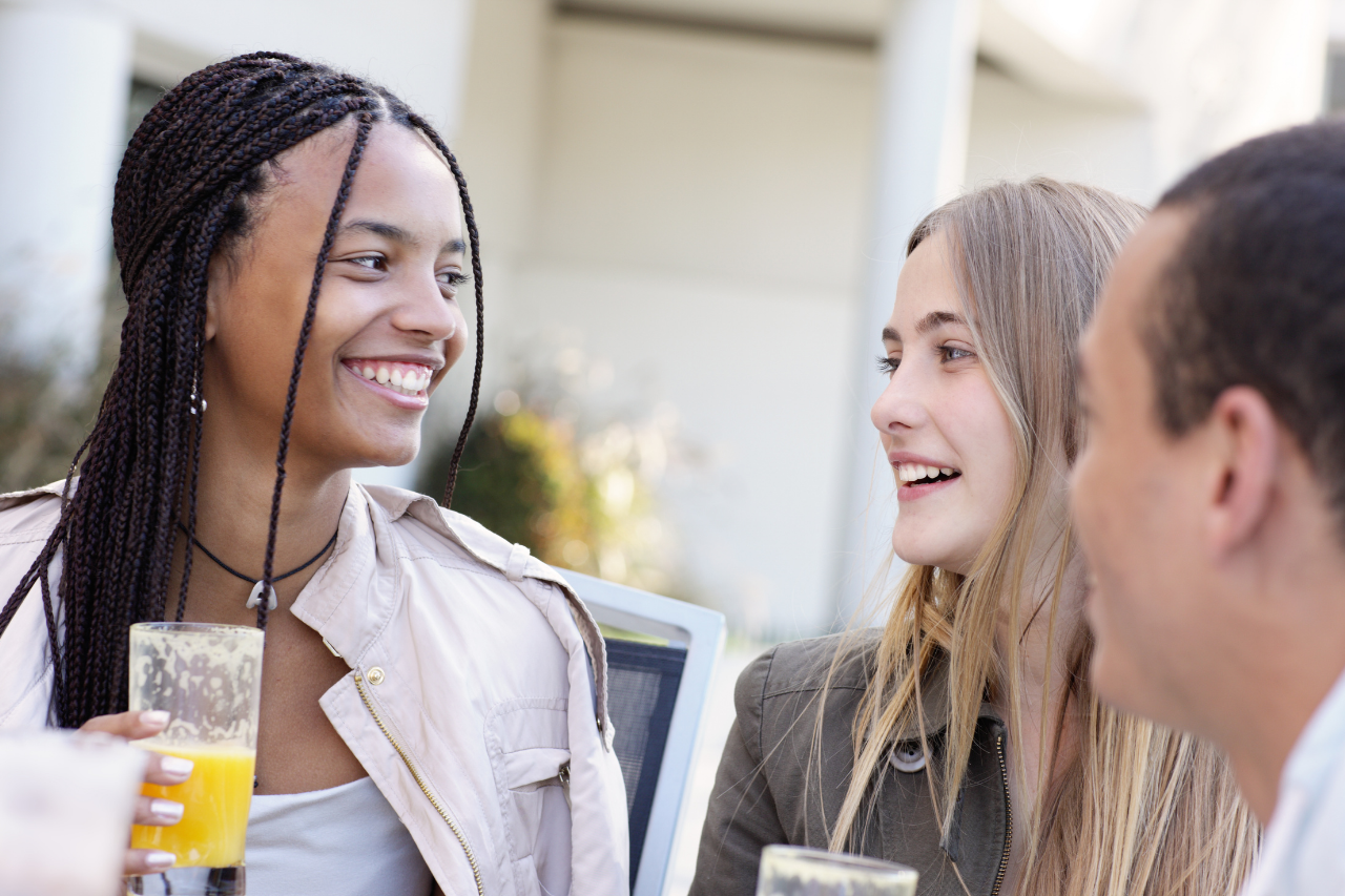 A woman smiling with a glass of juice in her hand along with two friends