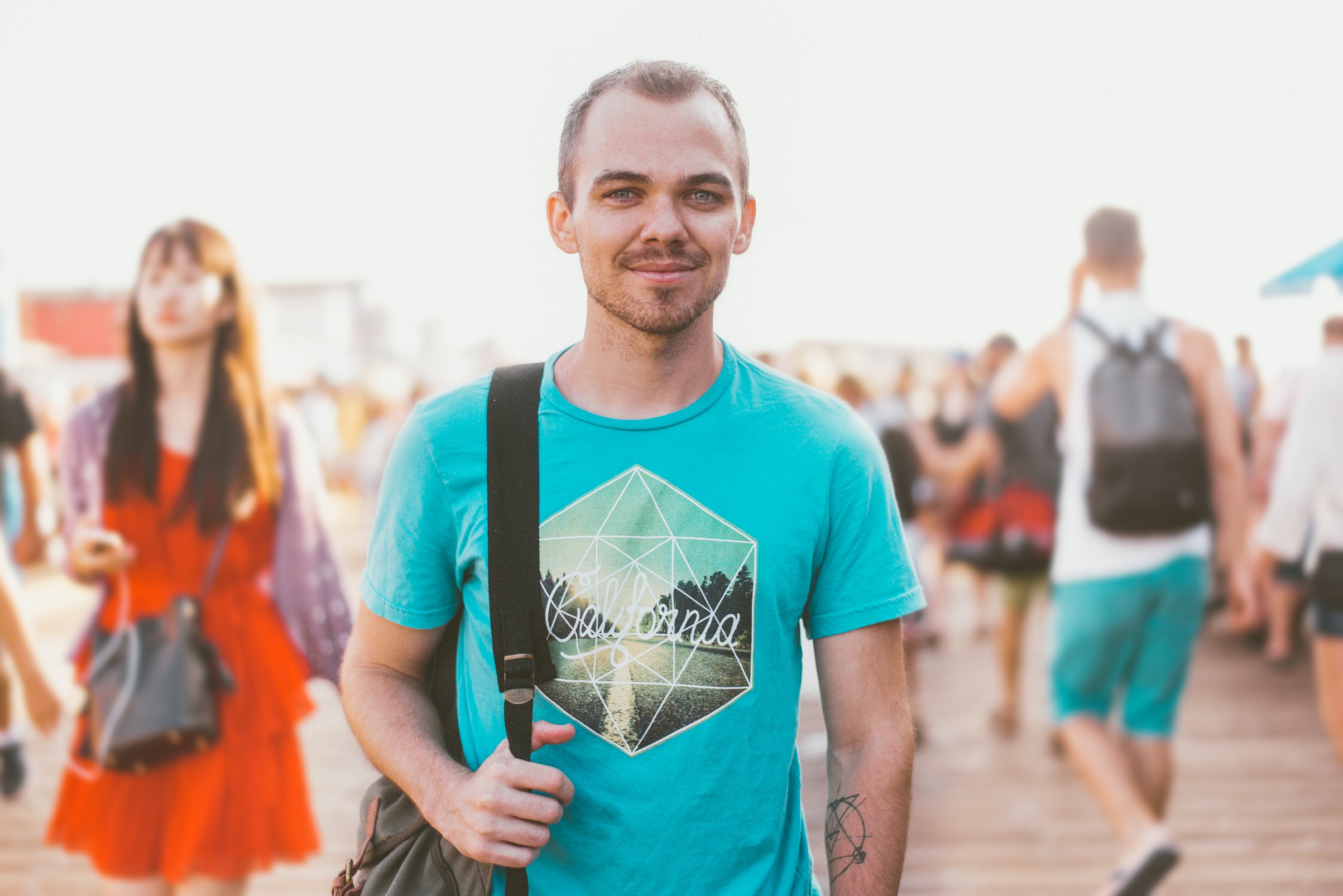 Man in a blue t-shirt and backpack smiling at the camera - university students