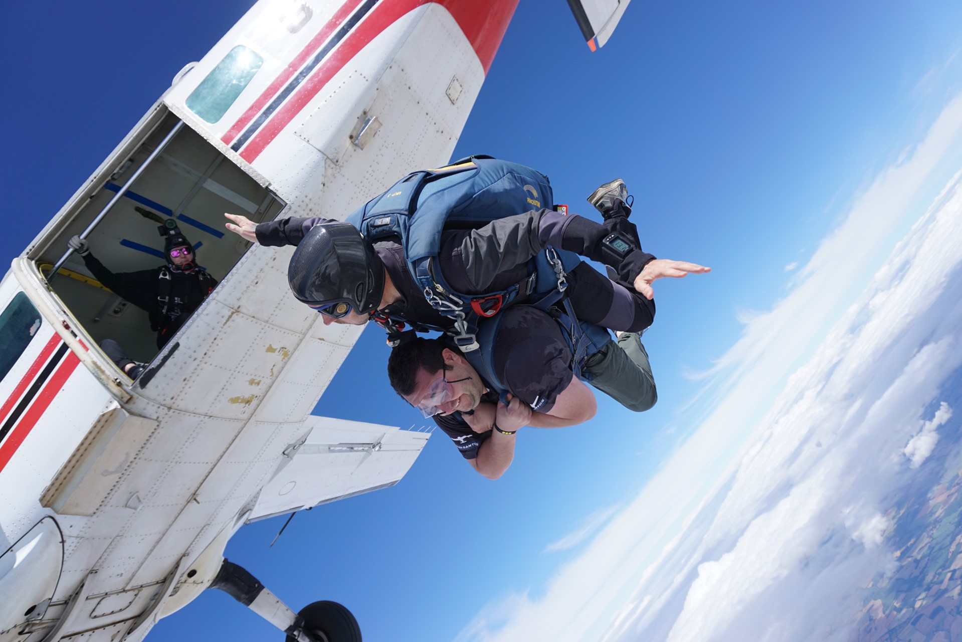 Two people skydiving out of a plane with the clouds below them. The person from Perkins is in a tandem with the instructor.