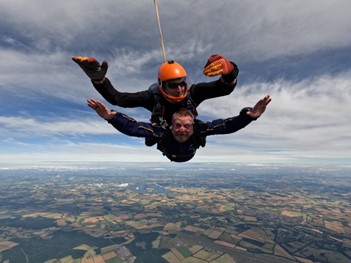 Two people, one of whom is from Perkins and the other who is an instructor skydiving out of a plane with a view of below