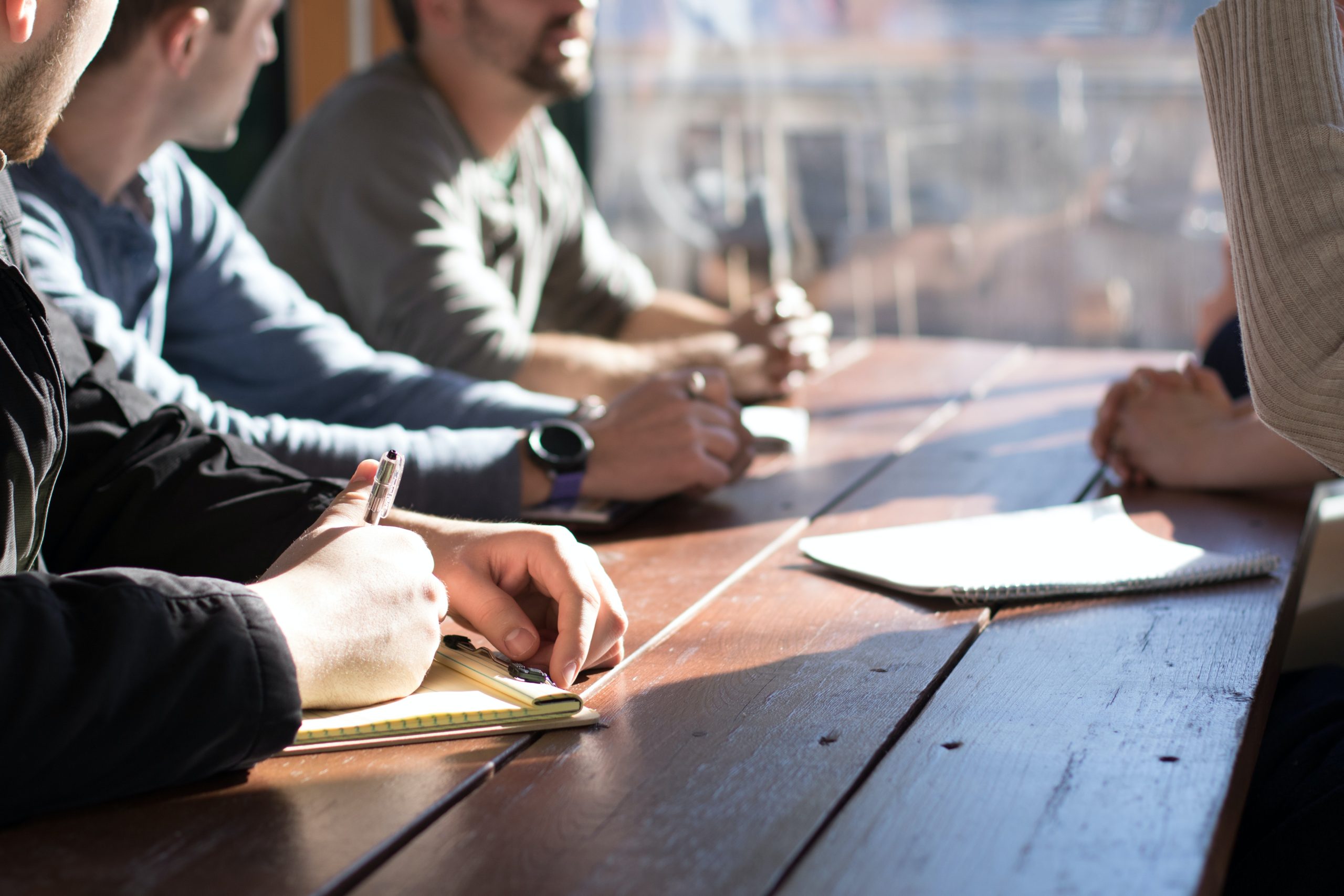 Four people sitting on a table writing notes on paper pads